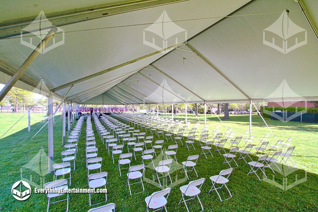 Interior view of a long 40x200 maxi-frame tent with rows of white chairs and staging set up on grass for a military ceremony by Everything Entertainment.