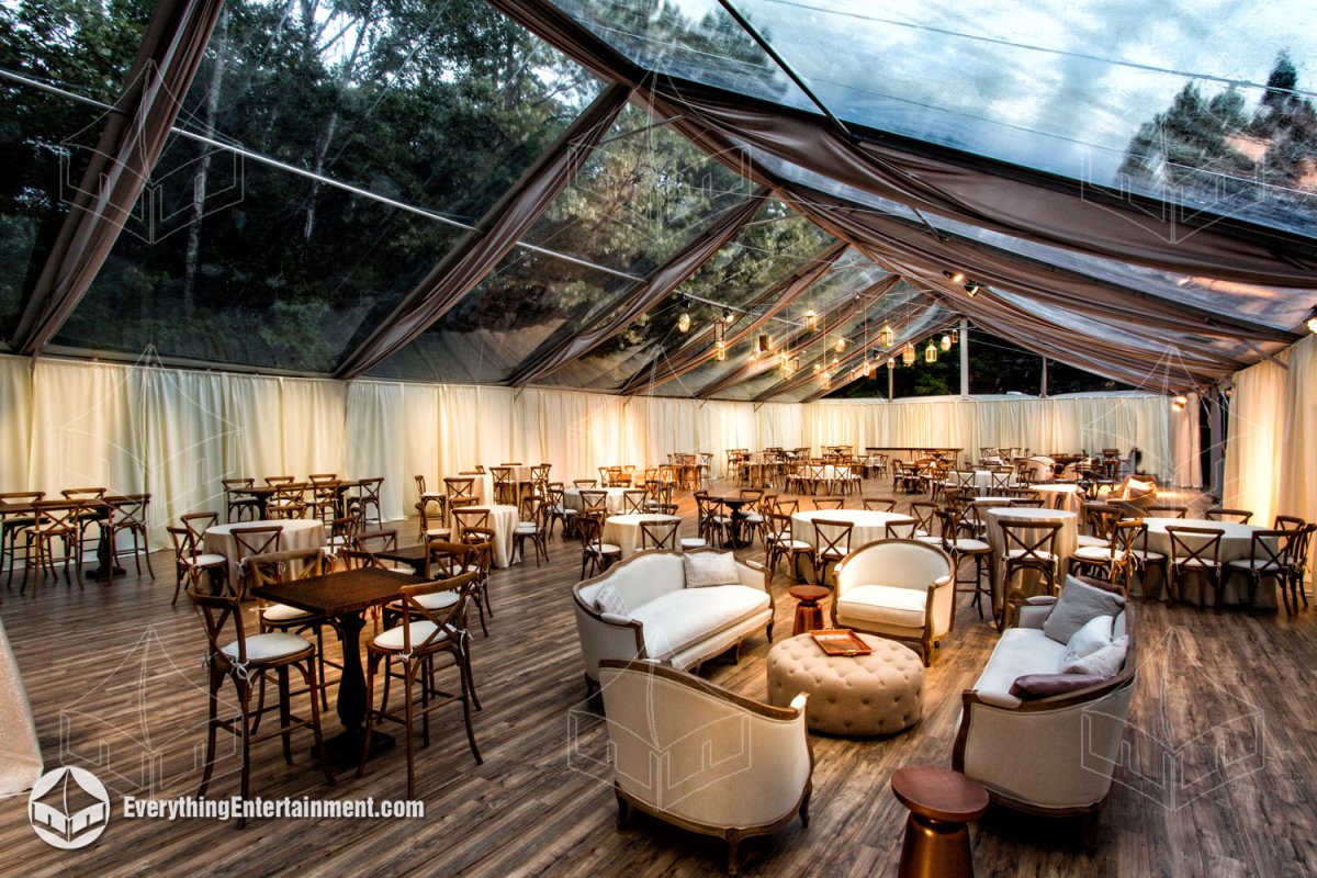 Interior view of a 50x100 clear top wedding tent with wood plank flooring, ceiling drape swags, and hanging lanterns installed on a tennis court in Upper Saddle River NJ by Everything Entertainment.