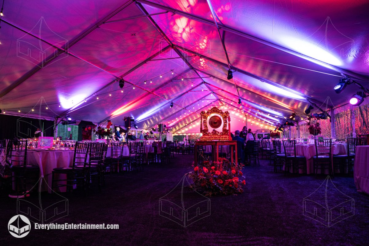 Gala setup inside a 50x120 frame tent featuring dark carpeted Dura-Trac subflooring, elaborate floral centerpieces, and theatrical uplighting by Everything Entertainment.