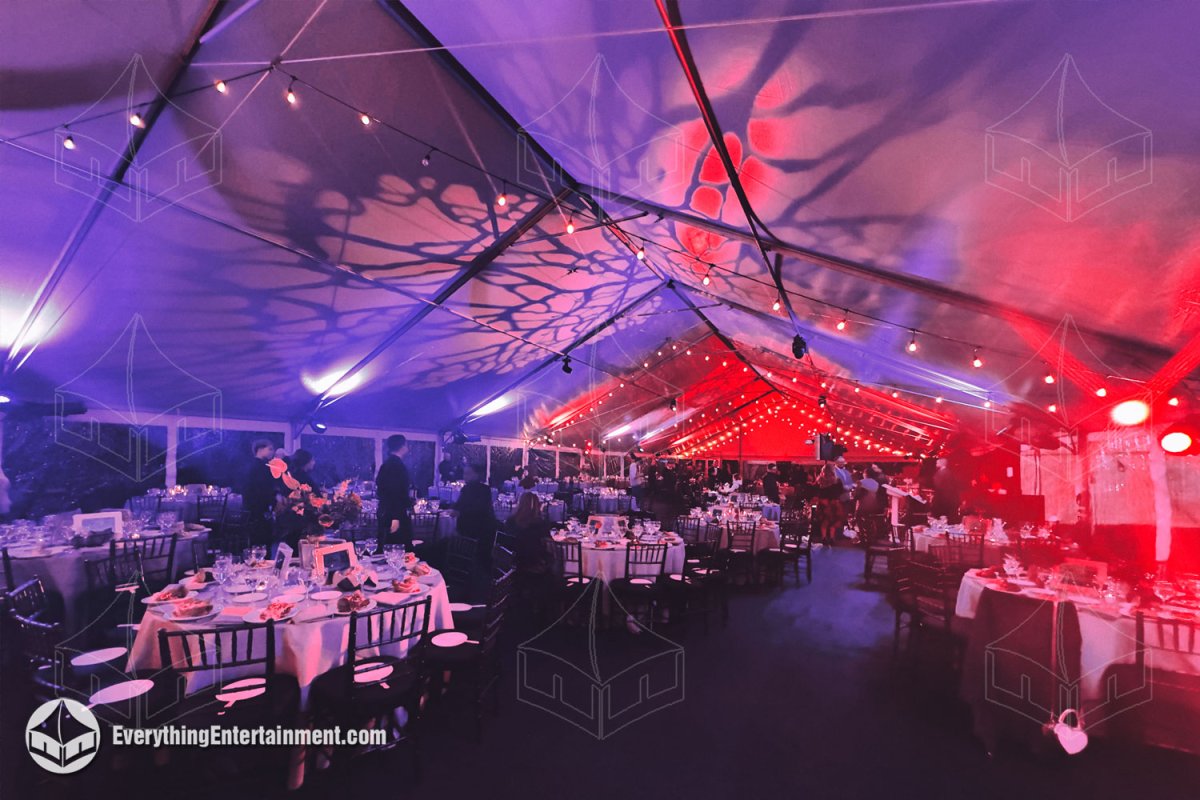 Interior view of a 50x120 maxi frame tent set with round dining tables and dramatic red and purple theatrical gobo lighting for the Neptune Ball at Snug Harbor by Everything Entertainment.