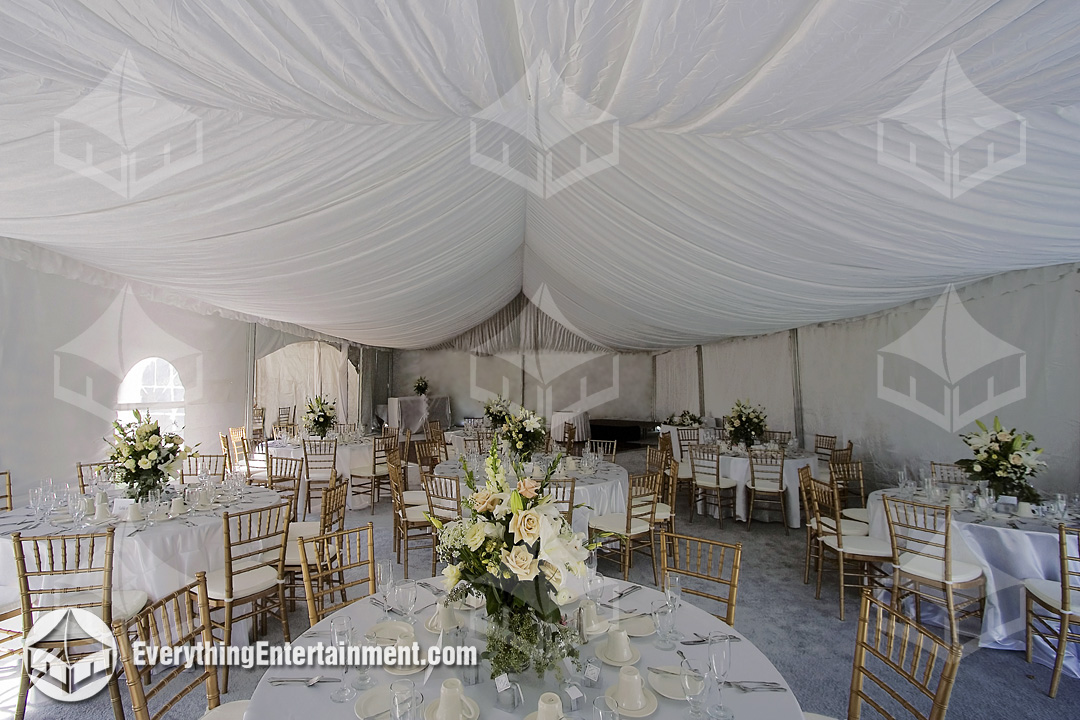Interior view of a draped wedding tent with tables and ballroom chairs
