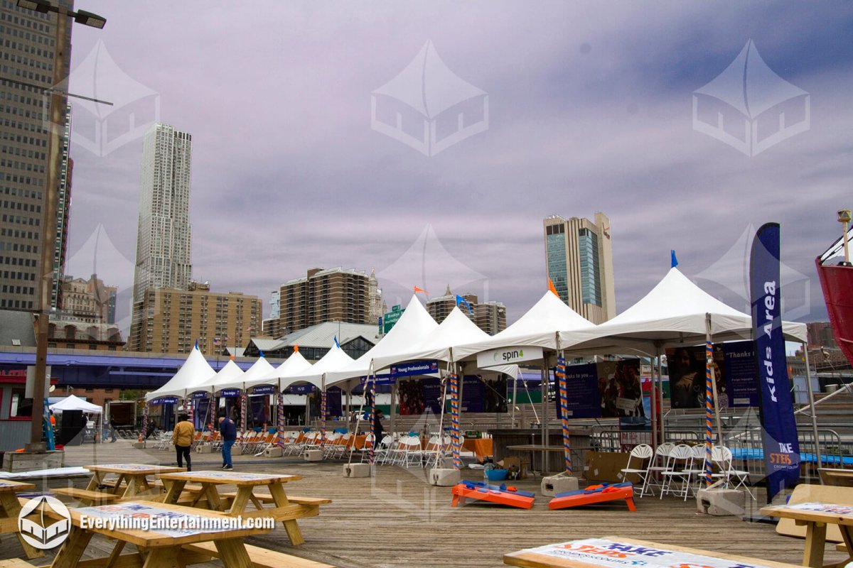 High-peak white tents and picnic tables set up by Everything Entertainment on the Pier 16 boardwalk at South Street Seaport, Manhattan.