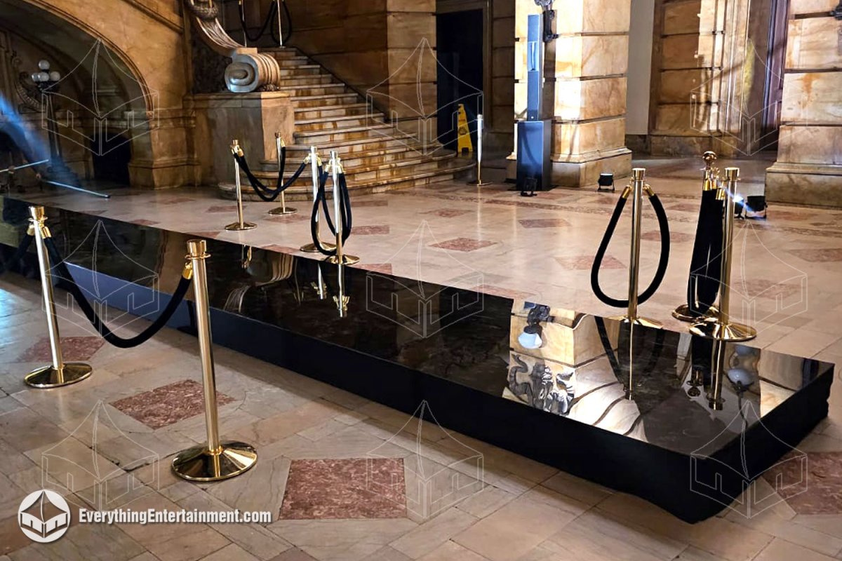 Custom high-gloss black acrylic topped runway stage with polished brass stanchions and black velvet ropes installed inside a landmark NYC venue for Fashion Week by Everything Entertainment.
