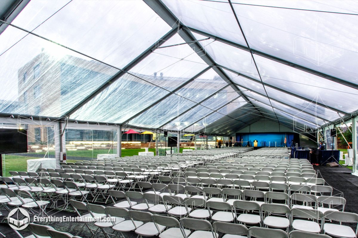 Wide interior view of a 50x200 clear top maxi-frame tent with a carpeted subfloor, presentation stage, and seating for 1,000 guests installed in Tarrytown NY by Everything Entertainment.