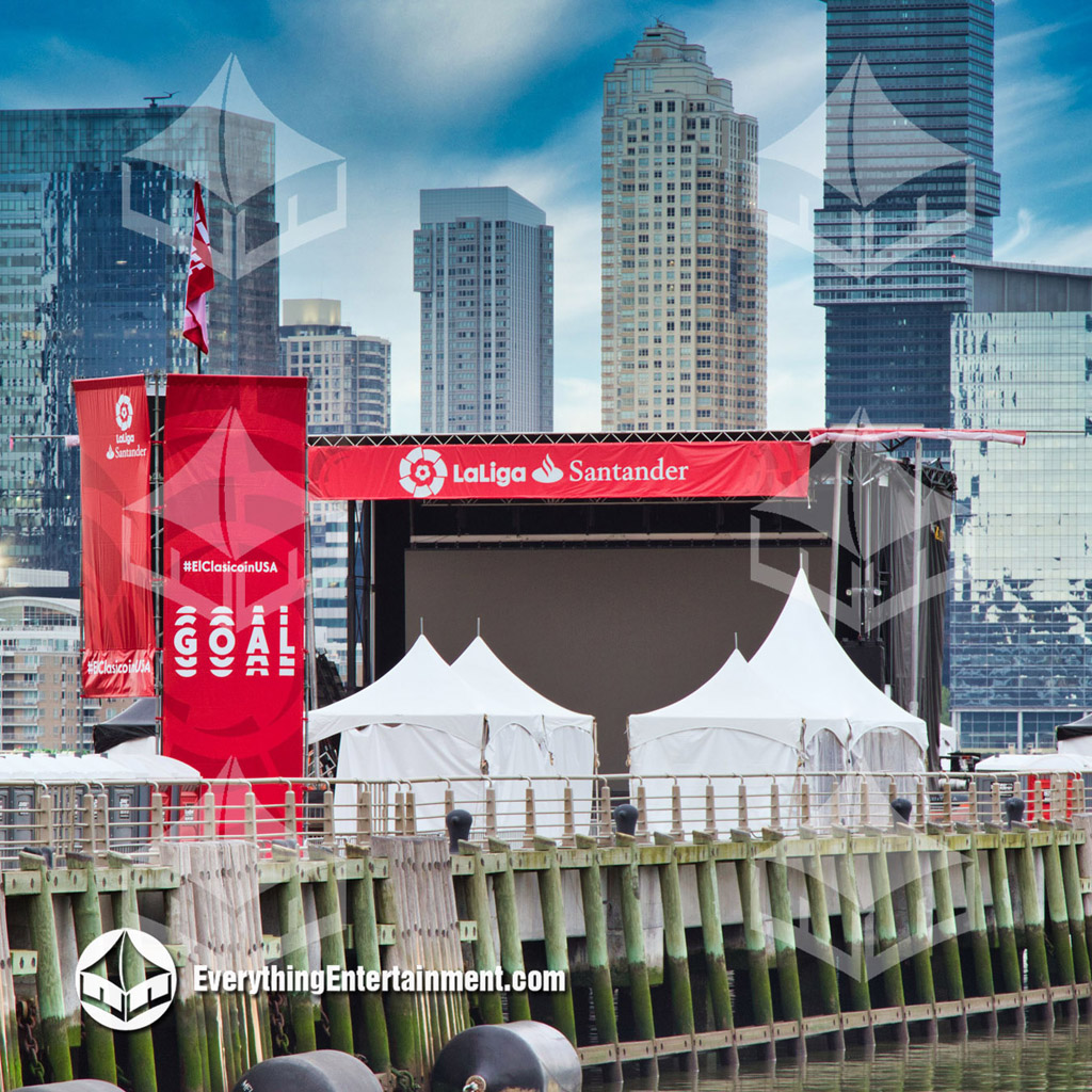 several high peak tents on pier in NYC with NJ skyline in background.