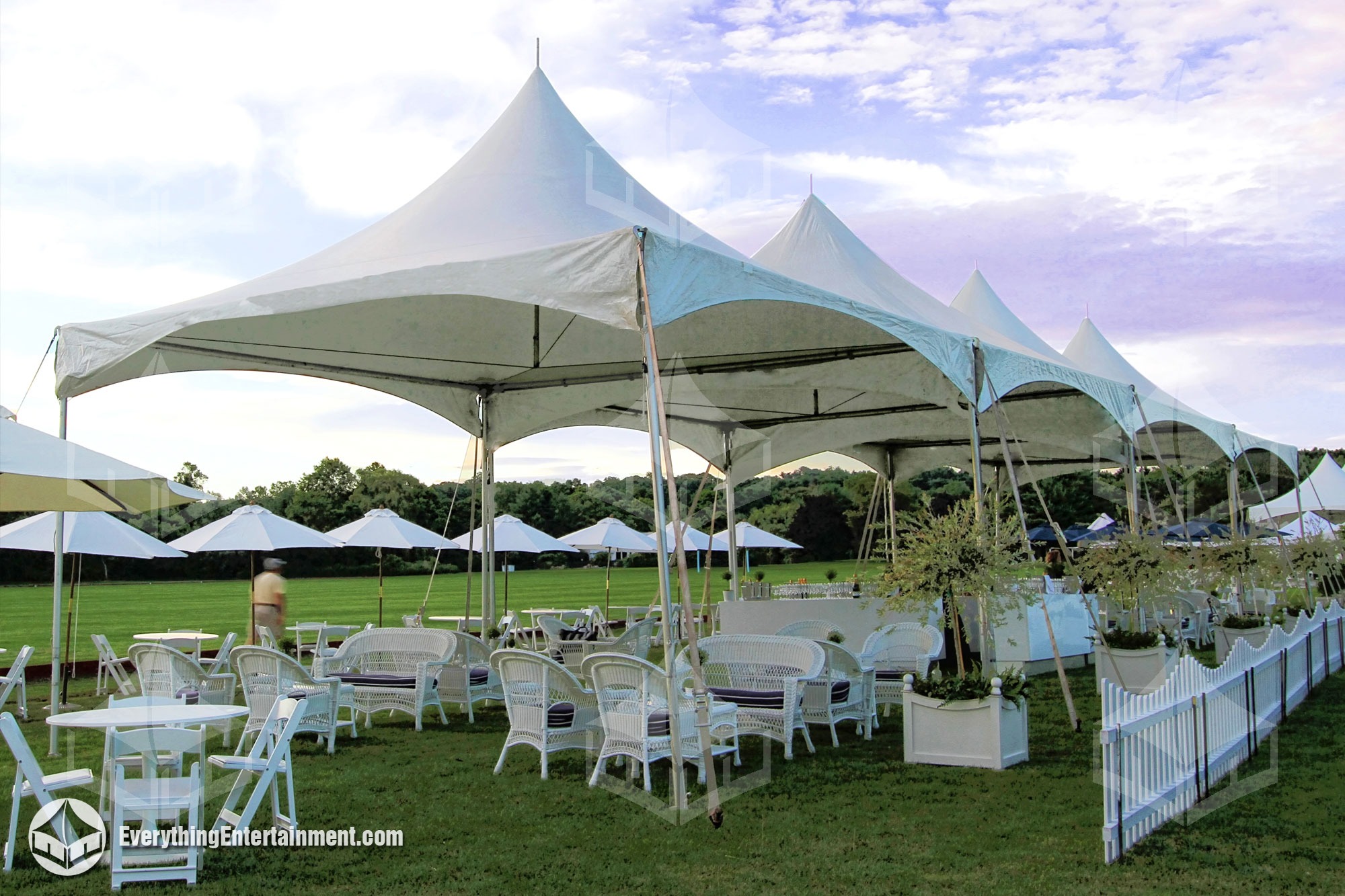 many high peak tents lined up in field with lounge furniture underneath