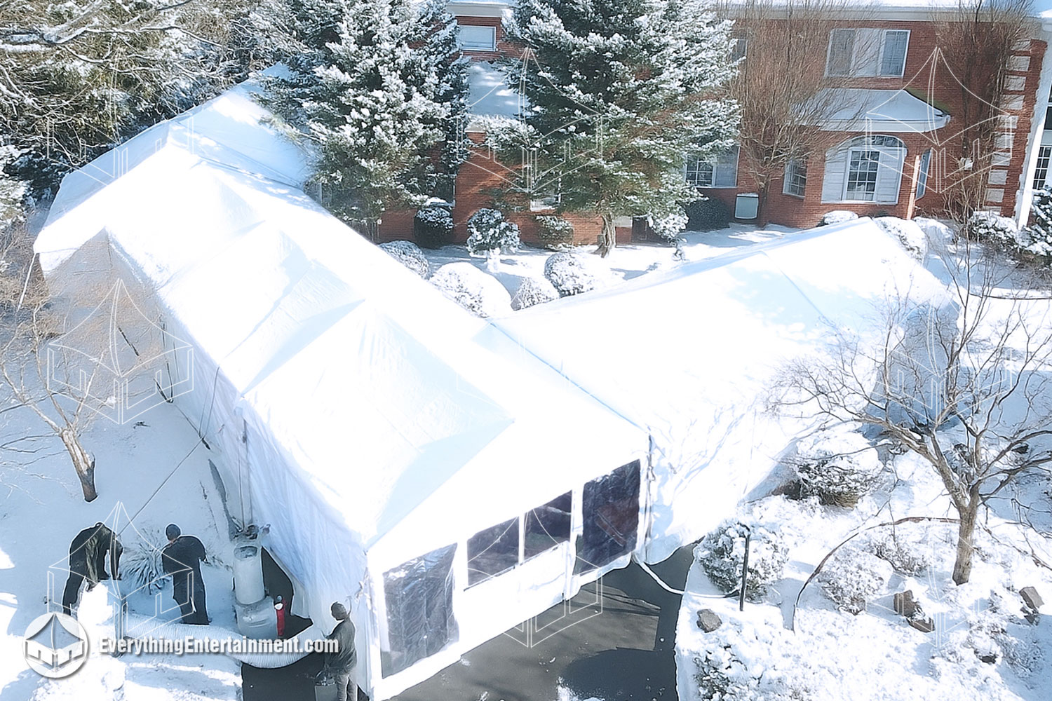 Multiple climate-controlled white frame tents beside a brick mansion during heavy snowfall, with the install crew inspecting tension cables in NJ winter.