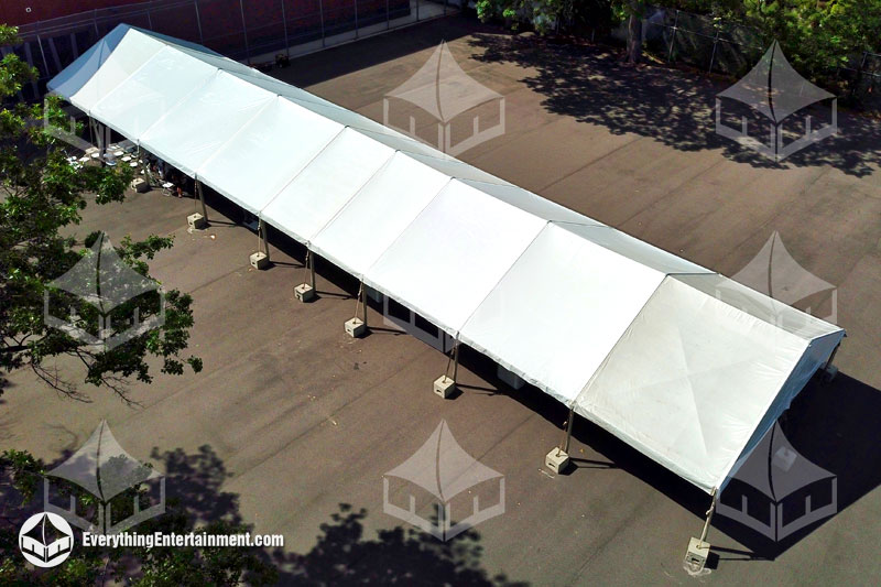 A long 30x125-foot frame tent rental setup with cement tent ballast in a schoolyard for commencement.