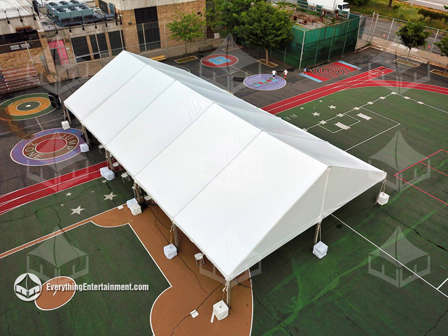 A large 40x75 foot frame tent rental setup with cement tent ballast in a school courtyard for graduation.