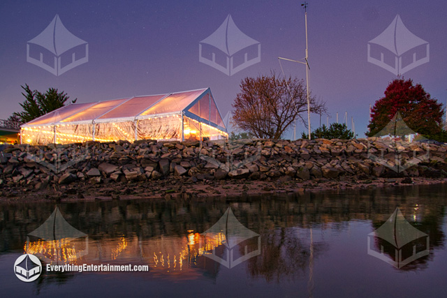 Lights are glowing through this clear top frame tent in the evening sky with reflections in the nearby ocean water.