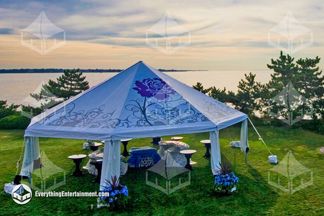 A Unique Octagon Shaped Tent Rental with a printed top setup on grass overlooking the water.