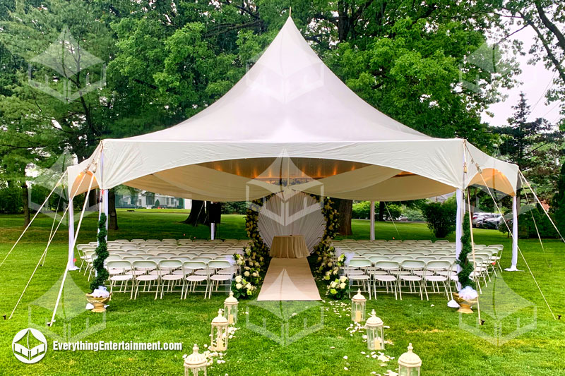 A high peak tent setup with chairs for wedding ceremony with lanterns and drapery