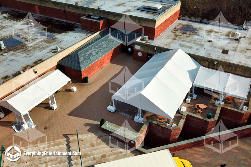 Multiple rental tents setup with cement ballast on paved courtyard for college food service.