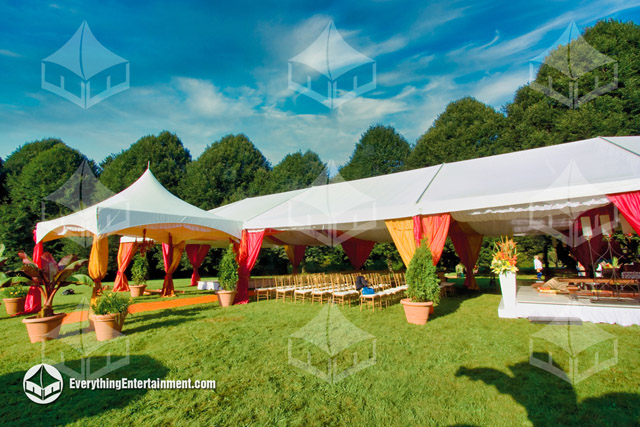 Engagement party tent with colorful drapery on grass backyard and trees in background.