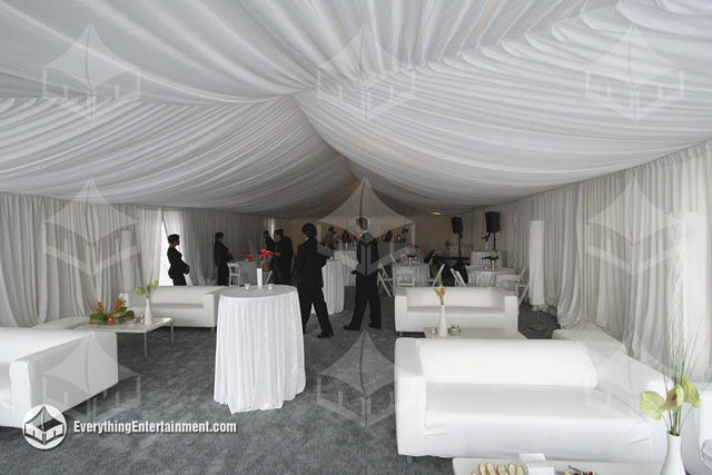Tent with white drapery, a white fabric tent liner, grey carpet, and lounge decor