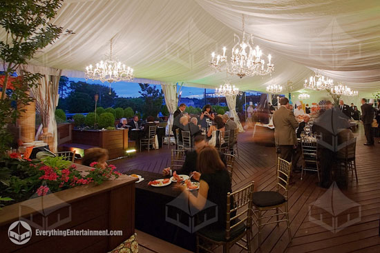 Wedding tent with large crystal chandeliers and white fabric drapery throughout the tent.