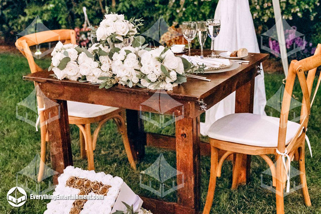 A small farm table with two cross-back farm chairs with lots of flowers.