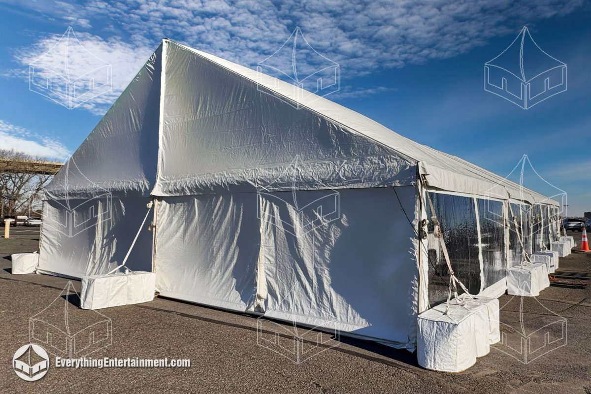 Exterior view of a long-term 40x60 white commercial frame tent ballasted with concrete weights on an asphalt lot by Everything Entertainment.