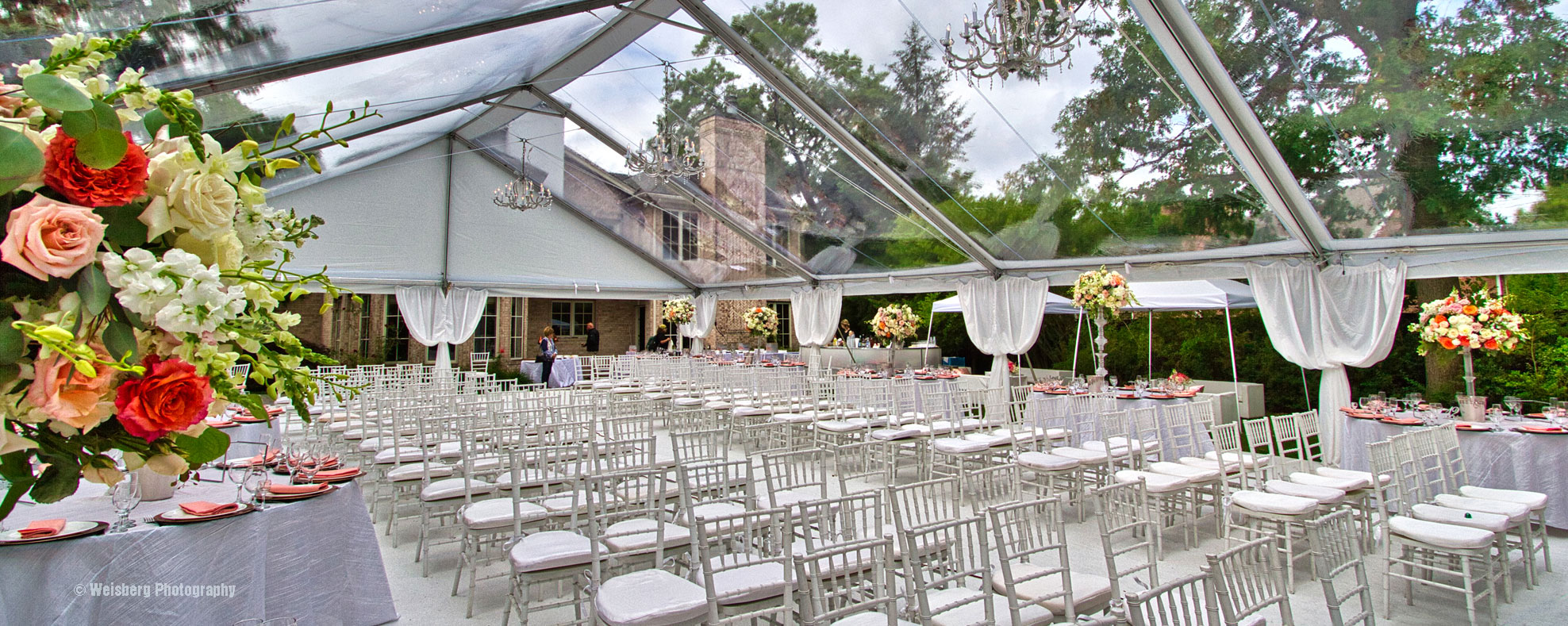 A large clear top frame tent with chairs set up for wedding ceremony