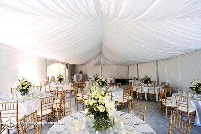 A wedding tent with fabric drapped top, gold ballroom chairs and tables fully set for a Middletown, NJ wedding.